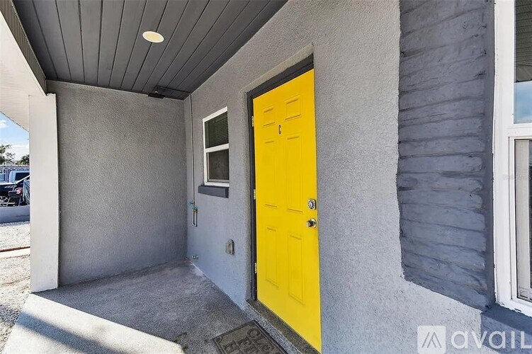 A yellow door is on the right side of a grey building.