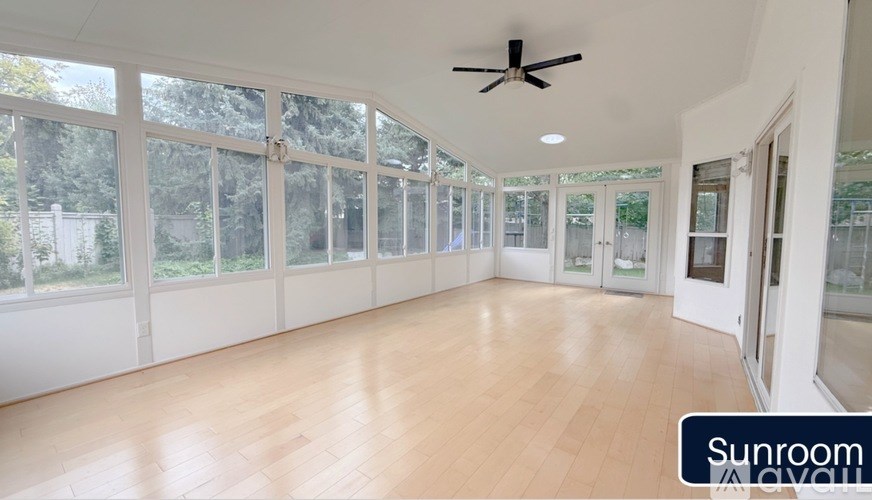 A sunroom with a ceiling fan and wooden flooring.