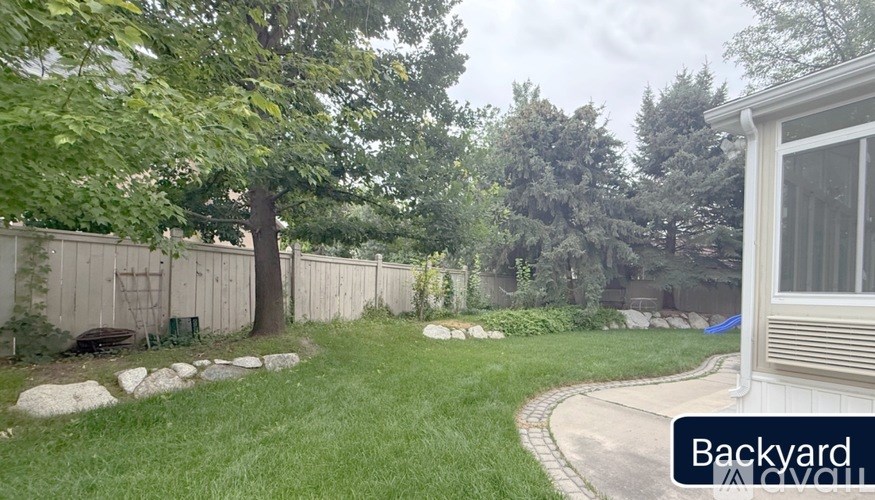 A backyard with a white house, a tree, and a fence.
