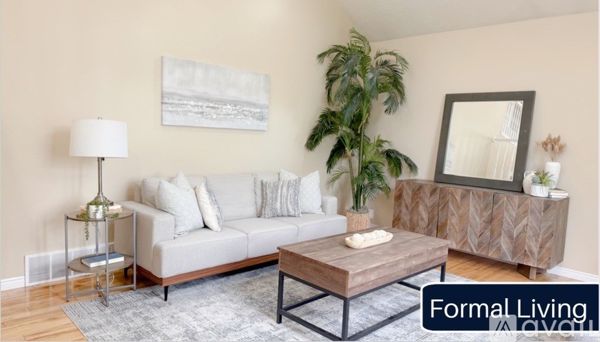 A living room with a grey couch, a wooden coffee table, a lamp, a potted plant, and a mirror on the wall.