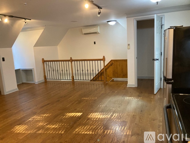 A spacious room with wooden floors and a staircase with a wooden railing.