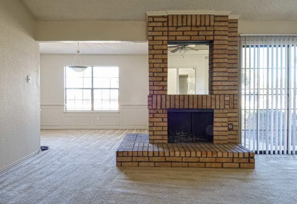 an empty living room with a brick fireplace and a mirror