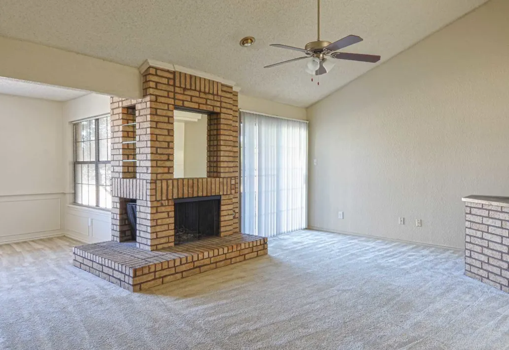 a living room with a brick fireplace and a ceiling fan