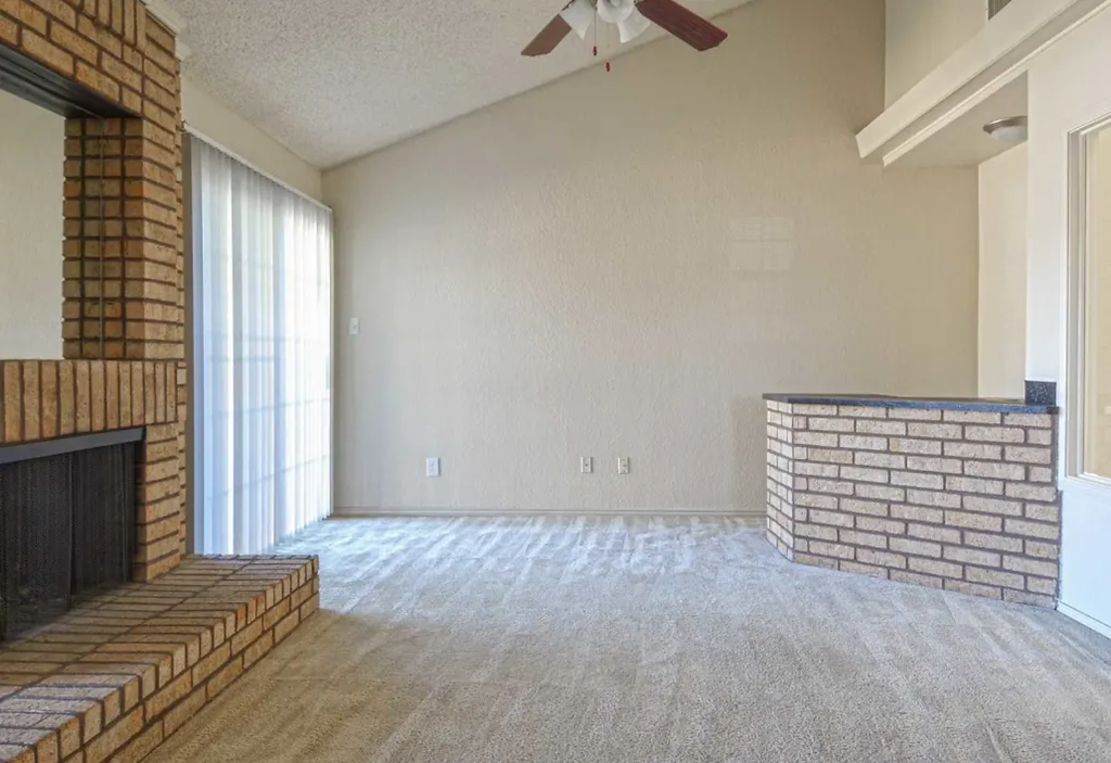 an empty living room with a fireplace and a ceiling fan