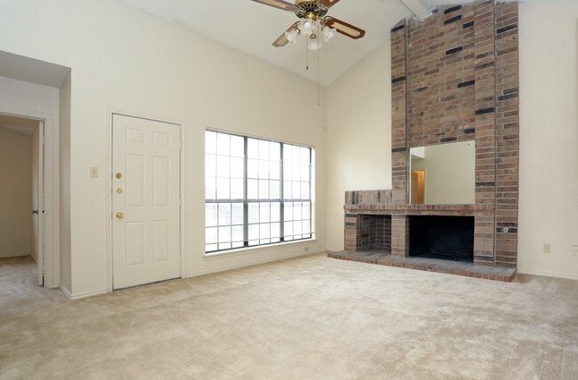 an empty living room with a fireplace and a ceiling fan