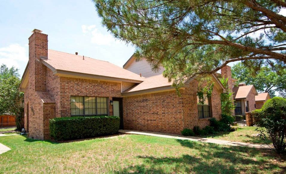 the front of a brick house with a yard and a tree