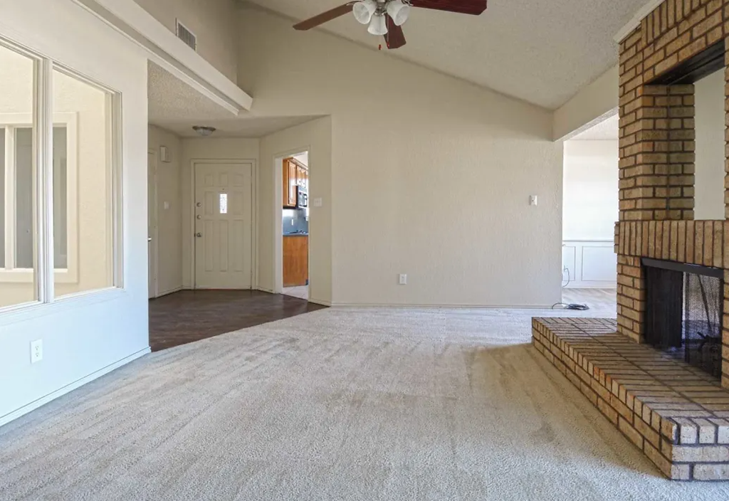 an empty living room with a fireplace and a ceiling fan