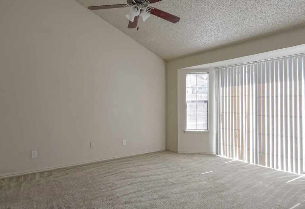 an empty living room with a ceiling fan and a window
