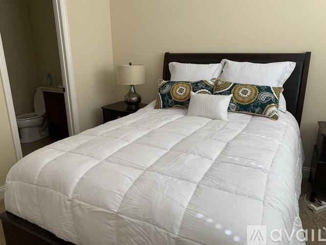 A bed with a white comforter and two decorative pillows.