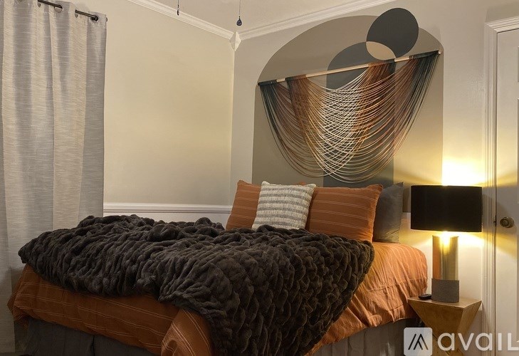 A bed with a brown blanket and pillows is in front of a wall with a circular decoration and a lamp.