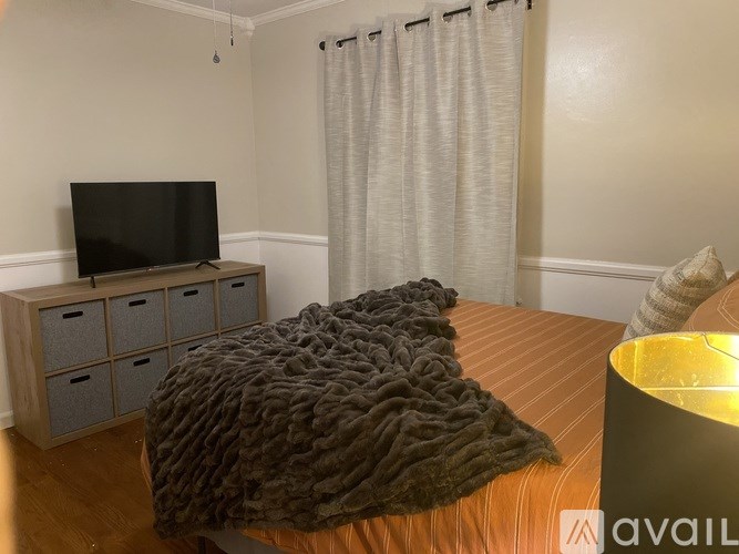 A bedroom with a bed covered in a dark blanket and a television on a wooden stand.