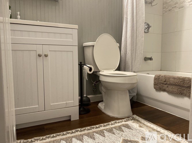 A white toilet sits in a bathroom next to a white cabinet and a white bathtub.