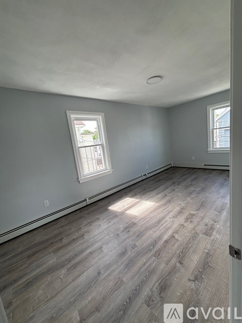 A room with wooden flooring and two windows.