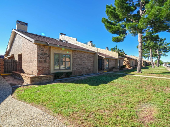 the front of a brick house with a lawn and trees