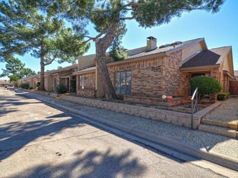 the front of a brick house with a street and trees