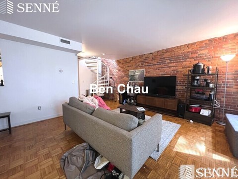 A living room with a couch and a television on a brick wall.