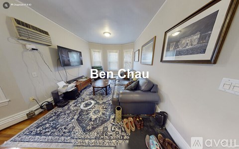 A living room with a blue rug and a television on the wall.