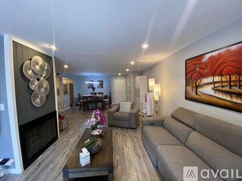 A modern living room with a grey sofa, a coffee table, and a painting of red trees on the wall.