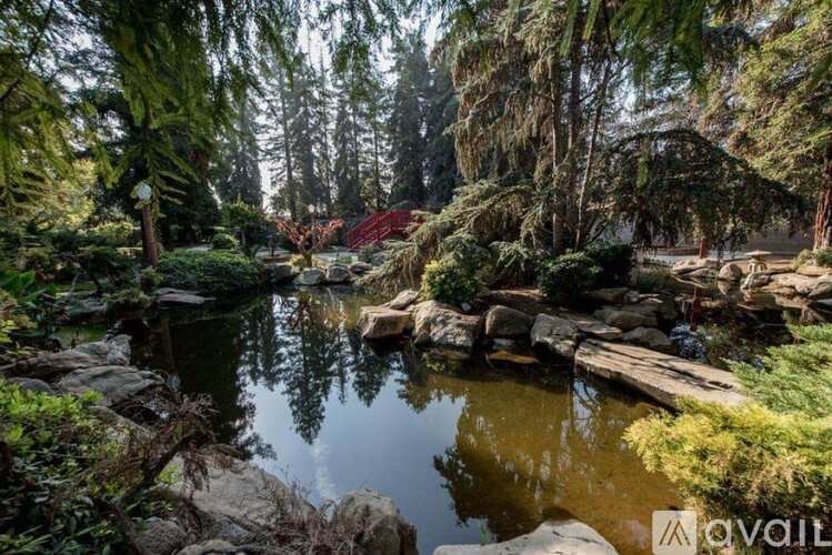 A tranquil garden scene with a pond, rocks, and trees.