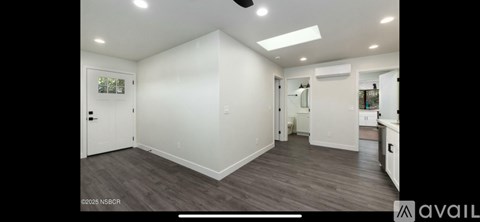A spacious room with a door on the left and a kitchen area on the right.