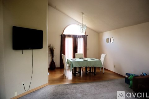 A living room with a television, a dining table with chairs, and a rug on the floor.
