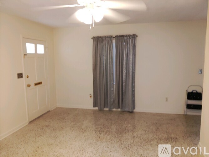 A room with a carpeted floor, a ceiling fan, and a window with curtains.
