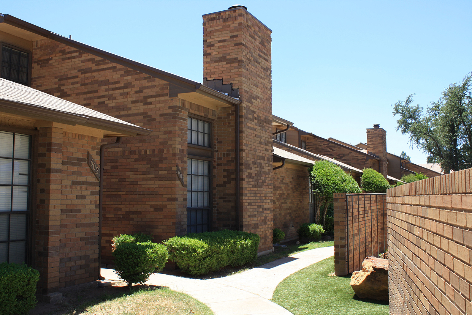 the side of a brick house with a sidewalk and a brick fence
