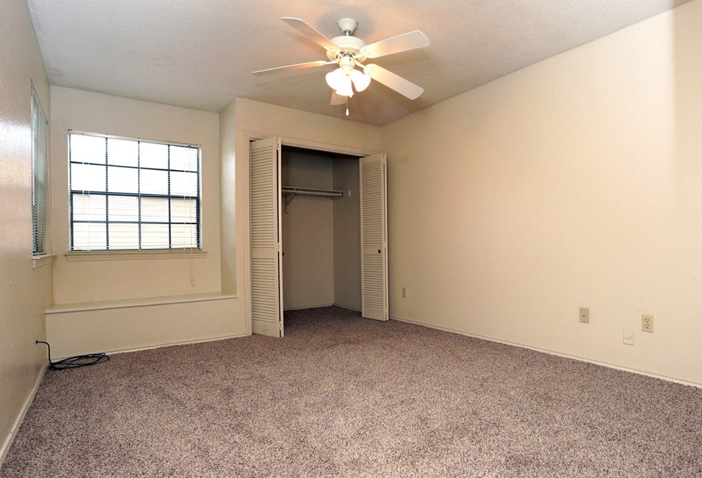 an empty living room with a ceiling fan and a closet