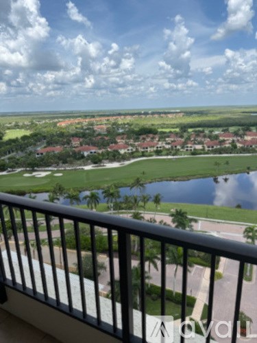 A balcony overlooks a green landscape with a body of water and a town in the distance.