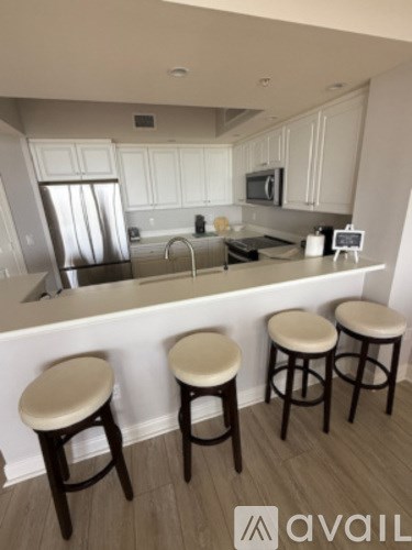 A kitchen with white cabinets and a bar area with four stools.