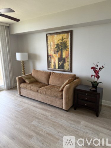 A living room with a couch, a painting, a lamp, and a vase of flowers.