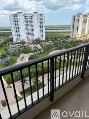 A balcony with a railing overlooks a green landscape and buildings.