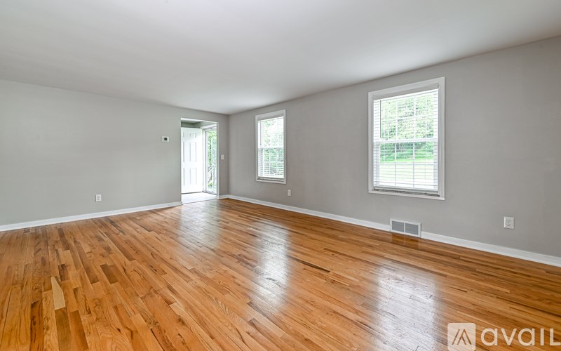 A room with wooden flooring and two windows.