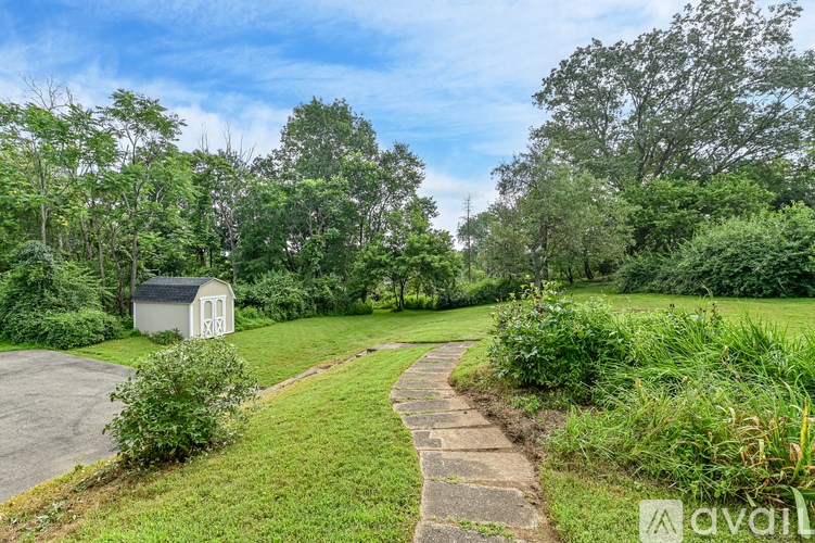 A small white shed sits in a grassy field with a stone path leading to it.