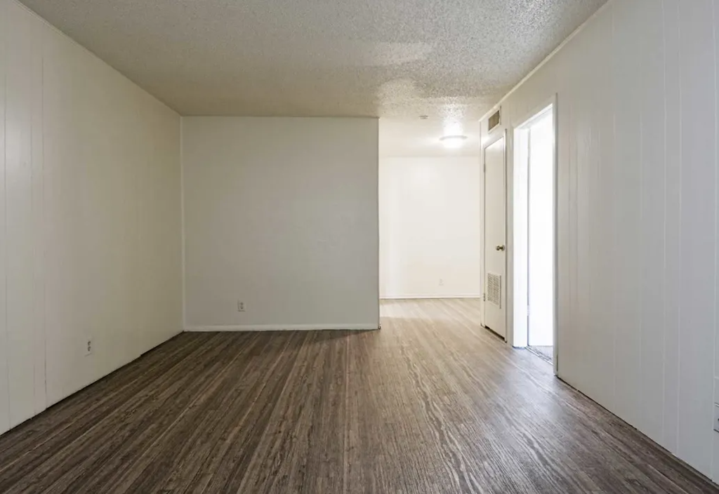 an empty living room with a wood floor and white walls