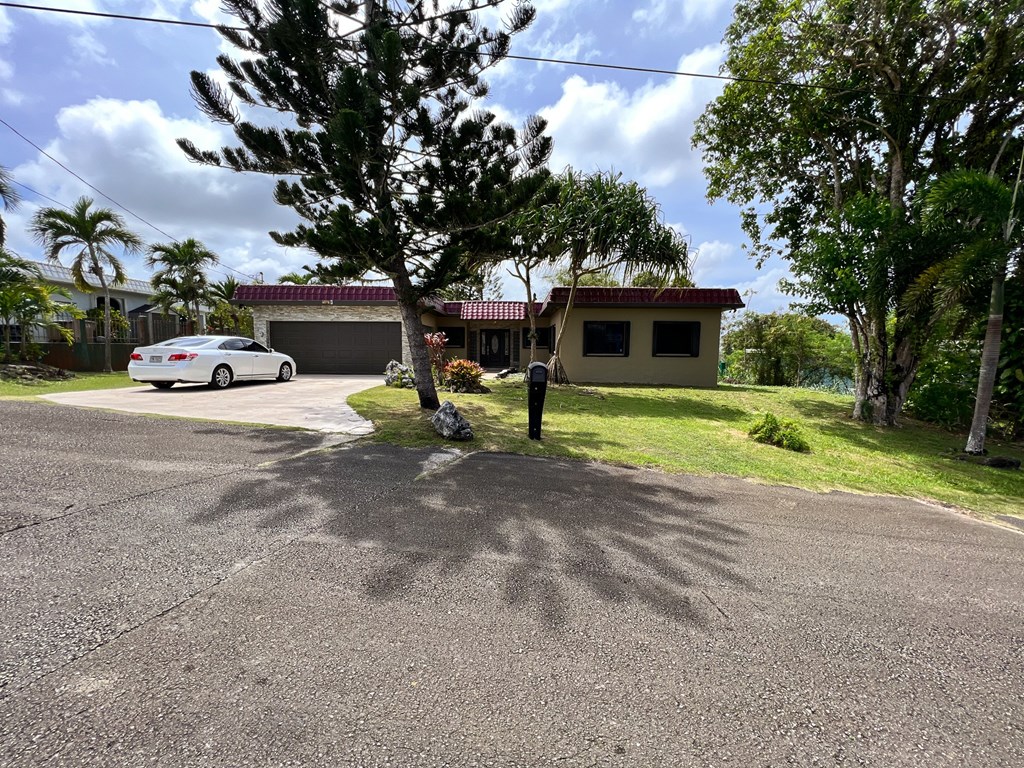 A white car is parked in front of a house with a tree in the foreground.