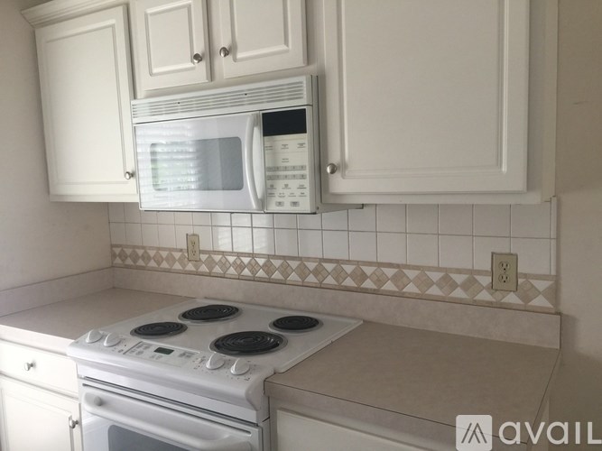 A white microwave is mounted above a white stove in a kitchen.