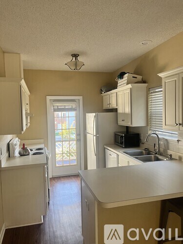 A kitchen with white cabinets and appliances, a window with blinds, and a chandelier hanging from the ceiling.