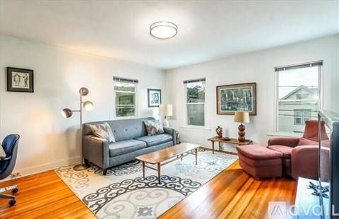 A living room with a grey couch, a red armchair, a wooden coffee table, and a rug with a black and white pattern.
