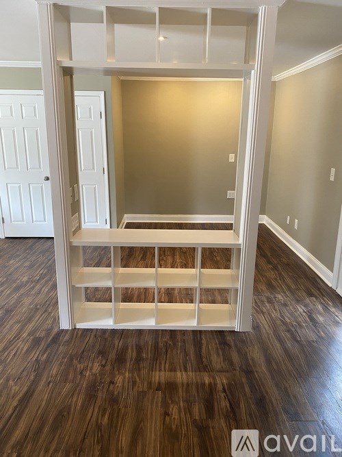 A room with a white built-in shelf unit and wooden flooring.
