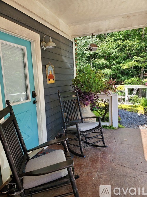 Two chairs are on a porch with a blue door.