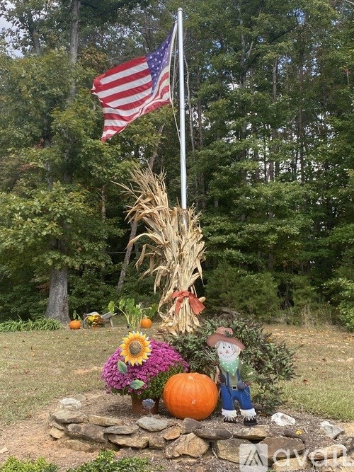 A small American flag flies above a decorative display of a scarecrow, pumpkin, and sunflower.