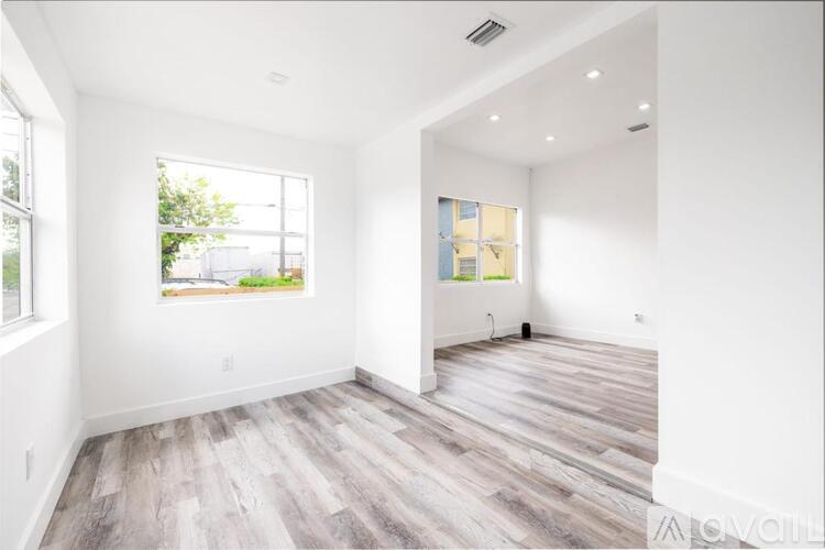 A spacious room with wood flooring and white walls.