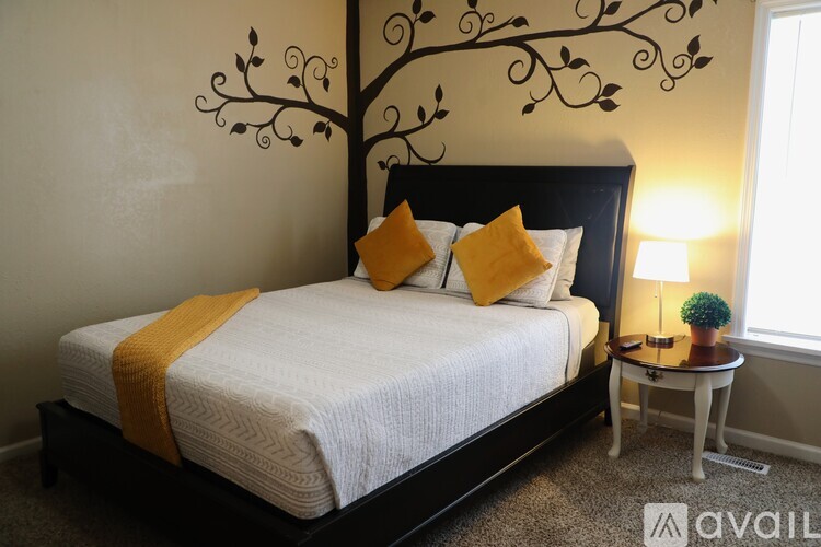 A bedroom with a white bed and a tree design on the wall.