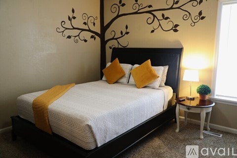 A bedroom with a white bed and a tree design on the wall.