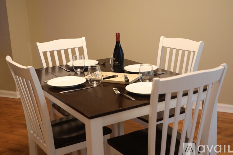 A dining table with white chairs and a bottle of wine on it.