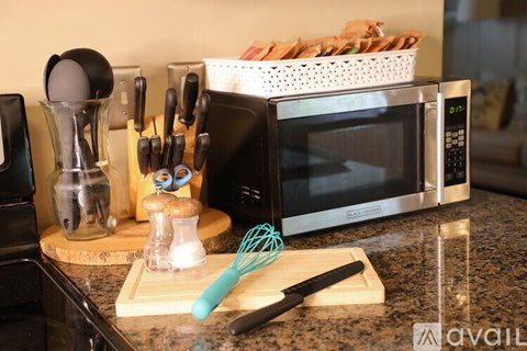 A kitchen counter with a black microwave, a whisk, a spatula, and a cutting board.