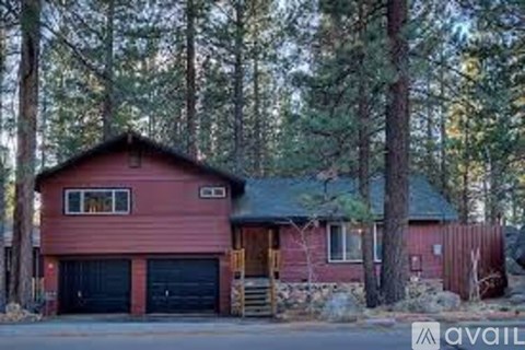 A red house with a black garage door is surrounded by trees.