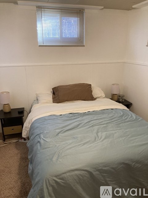 A bed with a blue comforter and white pillows is in a room with a window.
