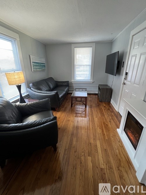 A living room with a black leather couch and a wooden floor.